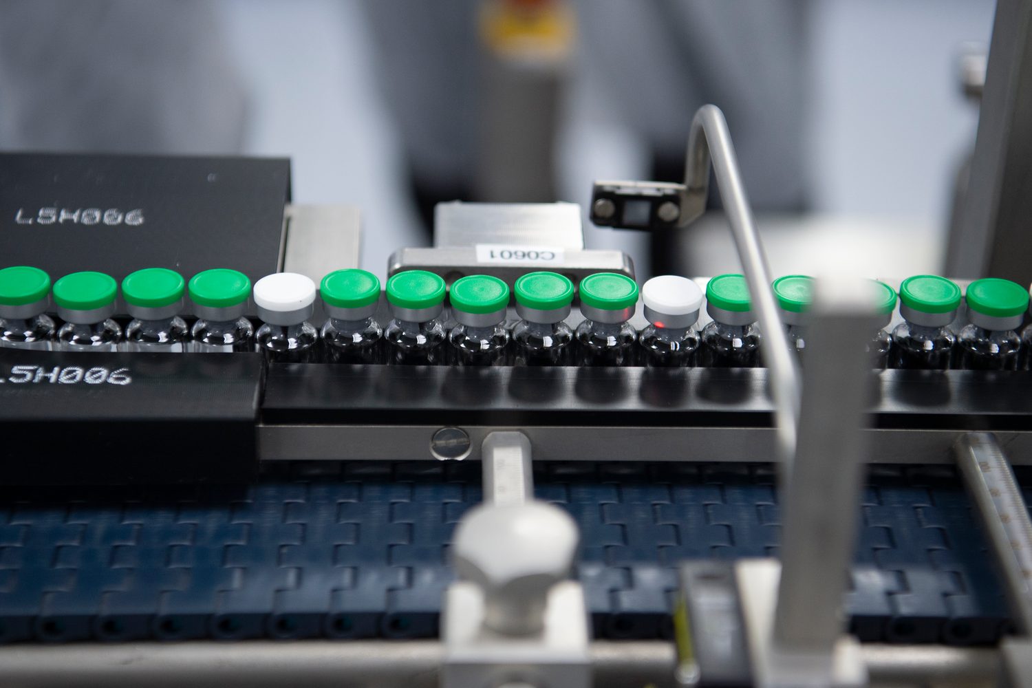 Rows of capped medicine vials moving along a pharmaceutical production line, tagged with batch codes.