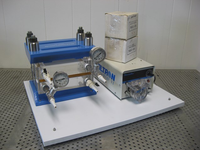 A tangential-flow filtration cassette holder with clamped membrane cassettes, pressure gauges, and a pump unit on a benchtop skid.